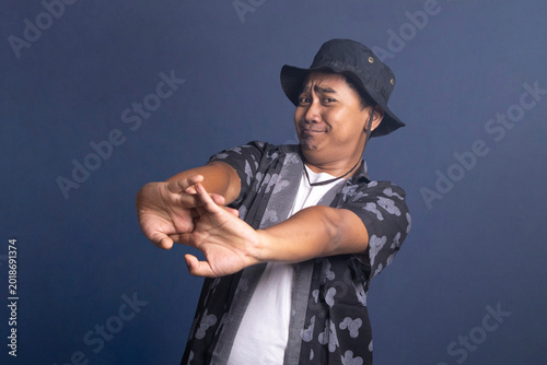 Bild auf Leinwand Young man wearing a black bucket hat and patterned shirt stretching his arms forward with interlocking fingers while making a tired or reluctant facial expression