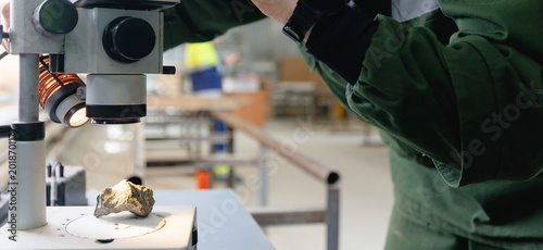 Foto Male scientist examining rock sample under microscope in industrial geology lab