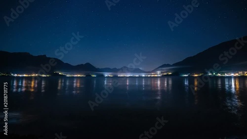 Stunning Nightscape: Tranquil Lake Reflecting City Lights and Starry Sky Between Mountains