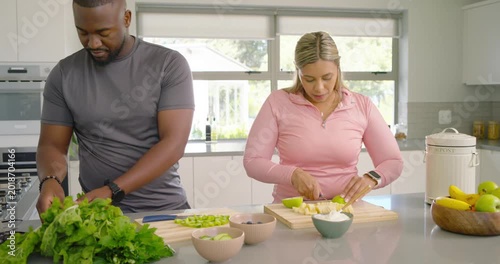 Couple starting salad prep at kitchen island chopping lettuce dicing fruit shifting lettuce smiling