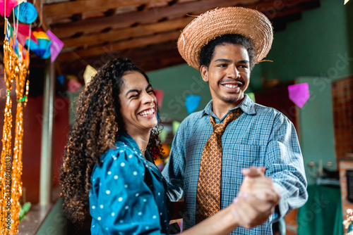 Happy young Brazilian couple dancing at a traditional Festa Junina celebration with colorful decorations.