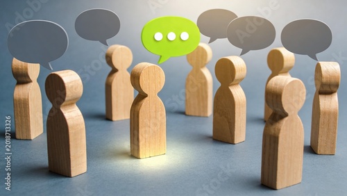 A group of wooden figures standing in a circle with one highlighted figure having a green speech bubble