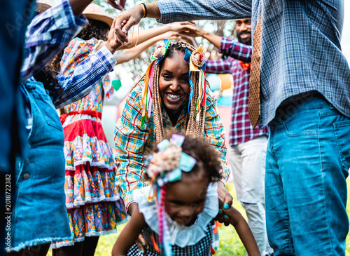 Happy Afro-Brazilian family celebrating Festa Junina with traditional dance and colorful costumes in a backyard.