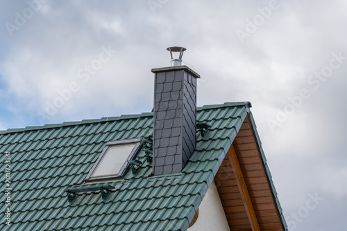 Green tiled roof with chimney and skylight. Overcast sky adds calm, quiet atmosphere. Ideal for home, architecture, or weather-themed projects