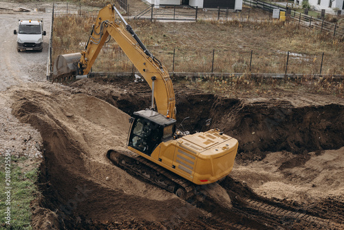 Orange excavator digging a foundation pit for residential building construction.