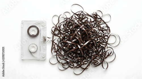 Plakat w ramie Transparent audio cassette with brown magnetic tape unspooled and tangled in a messy heap on a white background, representing retro technology failure.