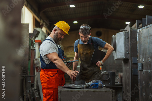 Bild auf Leinwand Metalworkers discussing manufacturing process in industrial factory