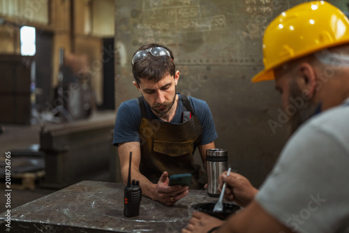 Obraz na plátně Young blue-collar worker taking break using smart phone