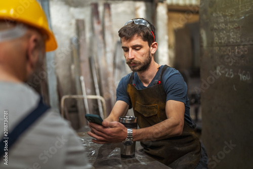 Obraz na plátně Young blue-collar worker taking break using smart phone
