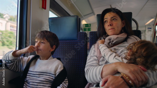 Valokuva Child sitting beside mother on train while she breastfeeds toddler creating real