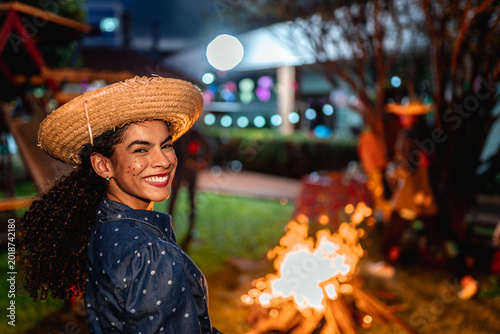 Photos Happy young woman in traditional caipira costume with straw hat smiling at a Festa Junina celebration at night near a bonfire