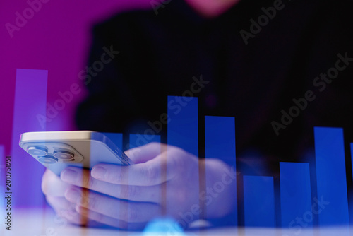 Person holds smartphone while looking at data charts during evening hours in a modern setting