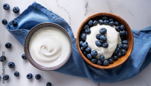top view of probiotic yogurt and milk kefir bowls with blueberries on white marble