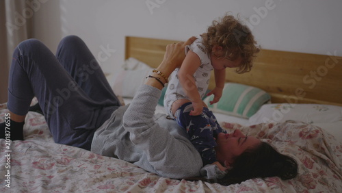 Photos Mother playing with toddler on bed in joyful morning moment as they laugh cuddle