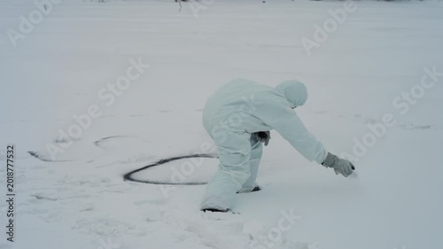 White suited technician draws dark circle on snowy ice marking recovery perimeter, bending to scrape snow away, scattered footprints, tense rescue atmosphere, overcast winter light