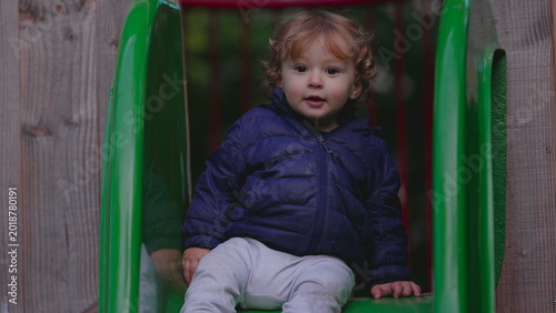 Canvas Print Toddler sitting at top of green slide hesitating to go down showing uncertainty