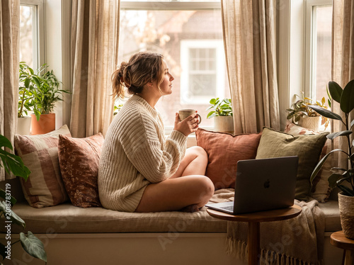 Young Professional Woman Sitting by Window with Coffee Cup Taking Break from Work Representing Work Life Balance and Mindful Remote Working