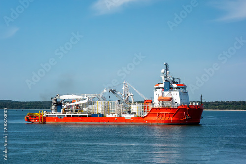 Schilderij op canvas A large red cable-laying ship, an offshore construction vessel for the energy industry, sailing in the blue sea on a sunny day