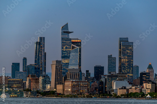 Hudson Yards Evening Skyline Across Hudson River. Evening view of Hudson Yards skyline across Hudson River with illuminated towers and open sky.