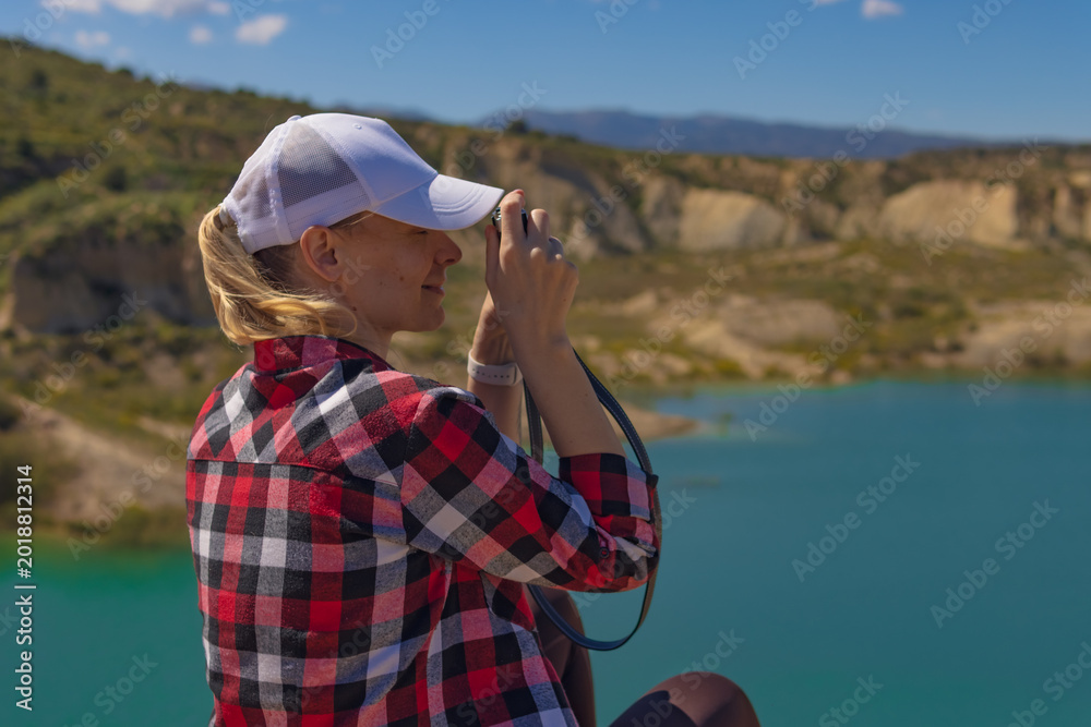 Fototapeta premium Woman traveling through nature, capturing the scenic landscape of clear blue lake and rugged mountains with vintage camera, enjoying adventure tourism and outdoor photography