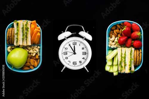 Luncn boxes and white alarm clock on a black background. Top view. Close-up.