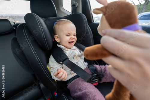 Foto Mother trying to entertain crying baby in car seat with a toy