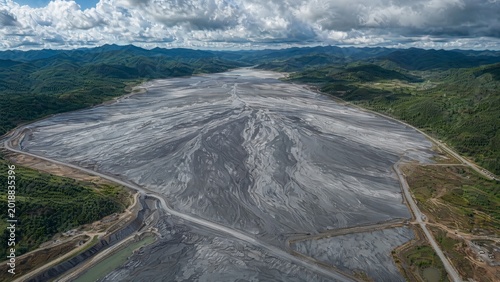 tailings. A vast, fan-shaped field of grey mine tailings contrasting with distant green hills. ESG reports, sustainability campaigns, designed for sustainability communications and ESG reporting.