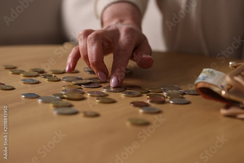 Pension. Senior woman counting coins at wooden table indoors, closeup