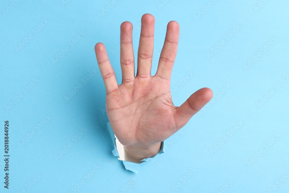 Naklejka premium Man showing palm through hole in light blue paper, closeup