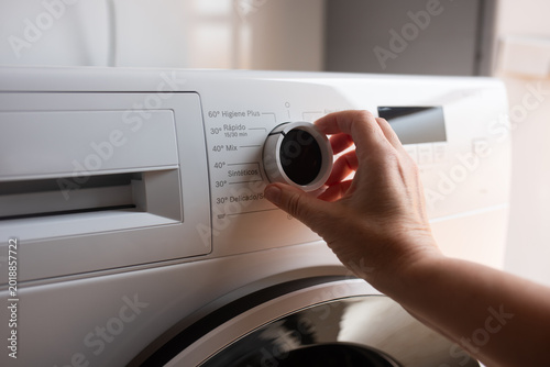 Person turning the program selector knob on a washing machine setting parameters for gentle laundry care.