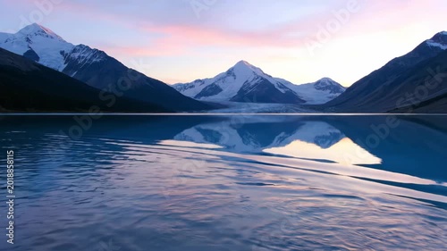Serene mountain landscape reflecting in calm lake waters at dawn, showcasing vibrant colors of sunrise illuminating snow-capped peaks and tranquil surroundings