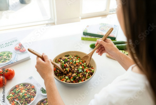Young woman tossing healthy pulse salad with wooden servers in bright modern kitchen