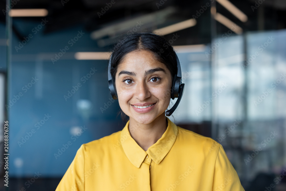 Fototapeta premium Close-up photo of a young Indian woman in a suit sitting in an office and smiling at the camera