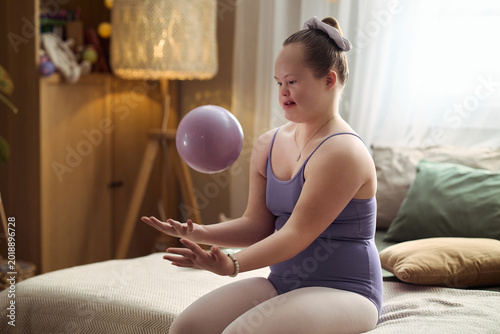 Cuadro en lienzo Caucasian girl with Down syndrome practicing coordination exercise with ball at home, showing inclusion and active lifestyle