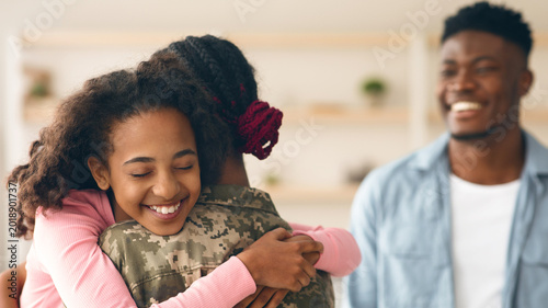 Bild auf Leinwand Two children embrace their military parent in a warm indoor space