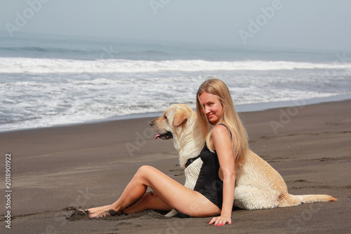 Photography Young blonde woman sitting with Labrador retriever on a tropical black sand beach in Guatemala