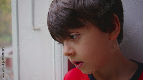 Schilderij op canvas Boy leaning toward window with pensive thoughtful expression mixed with quiet me