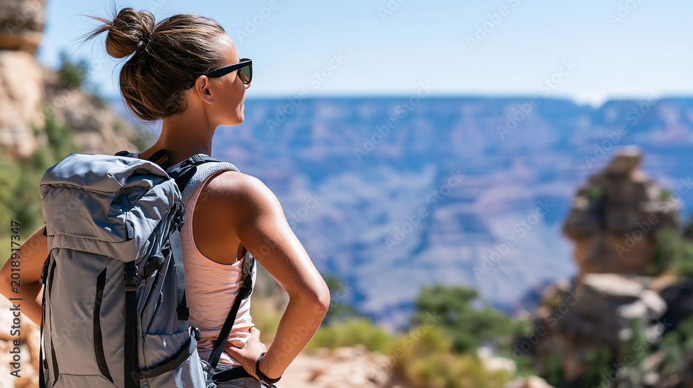 Naklejka premium Rear view of a woman hiking in the Grand Canyon, solo female hiker concept, Grand Canyon trail photography, Arizona adventure exploration, defocused background, with copy space