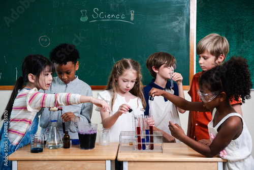 Diverse elementary students performing science experiment in classroom laboratory, exploring chemistry and teamwork. STEM education, curiosity, learning, innovation and child development concept.