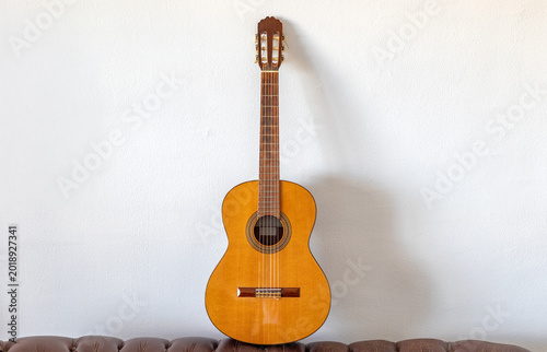 Classical acoustic guitar standing against white wall indoors