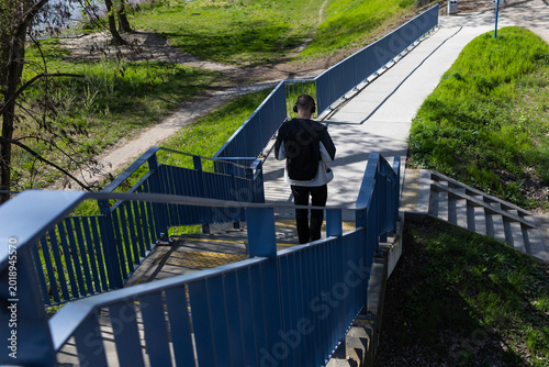 Schilderij op canvas Rear view of a young man walking on a pedestrian bridge in the park