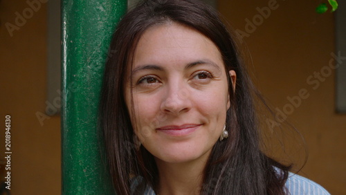 Konstfotografi Woman smiling warmly while leaning against green pole outdoors as gentle breeze