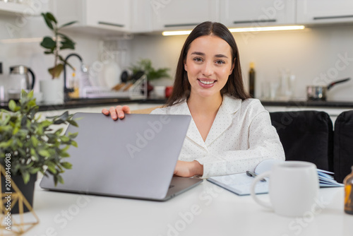 Fotografi Young woman at home closes laptop looks at camera smiles exhales in relief workday done calm