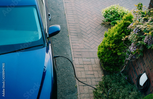 Top view electric car plugged into a charging station while parked in home. Residential EV Charging Station. Home EV Charging. Sustainable Power of a Wall-Mounted Charger. Future of Clean Transport.