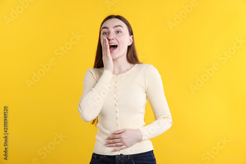 Young woman laughing at joke on yellow background