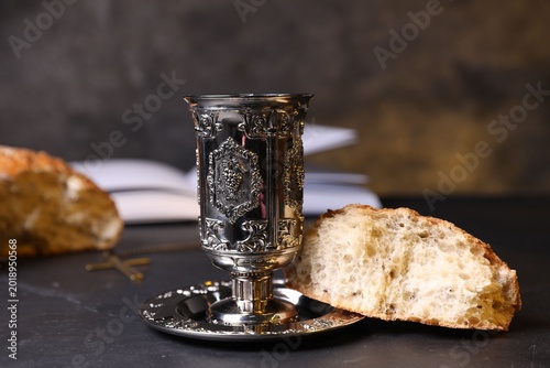 Holy Communion. Wine in cup, bread and Bible on black table, closeup