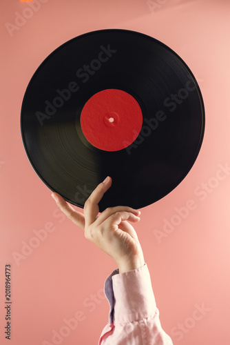 Hand holding a vintage vinyl record with a bright red label against a pastel background