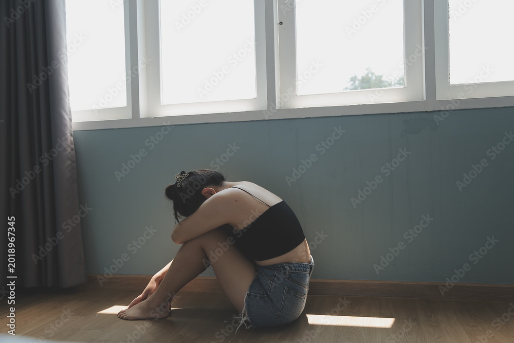 Fototapeta premium Woman sitting on floor in thoughtful pose near large window with natural light streaming in