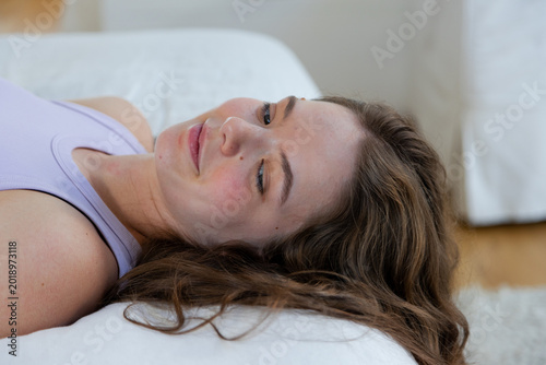Female lying horizontally across bed wearing lilac tank top, resting head on white pillow