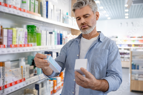 Fotografie Senior Caucasian man with gray hair holding medical product package and comparin